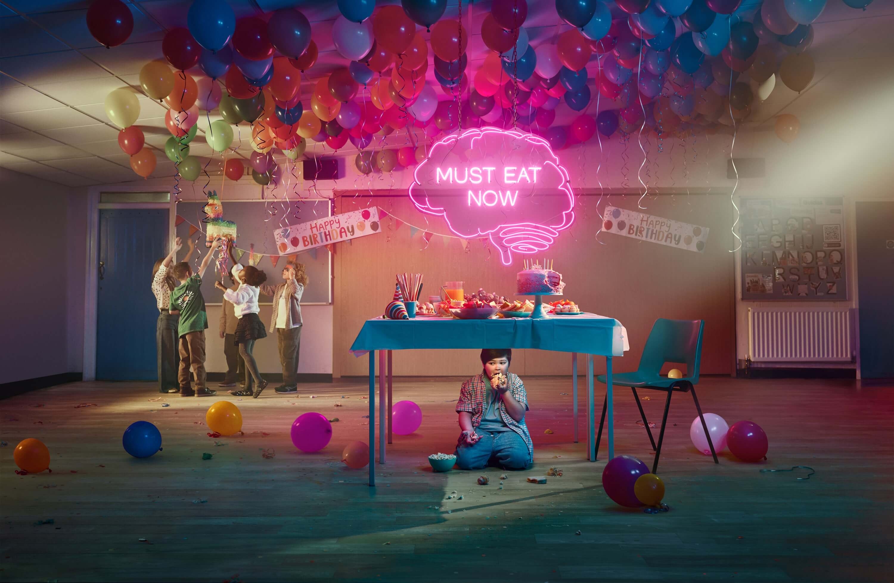 Boy sitting under a table and eating at a birthday party. Actor portrayal.