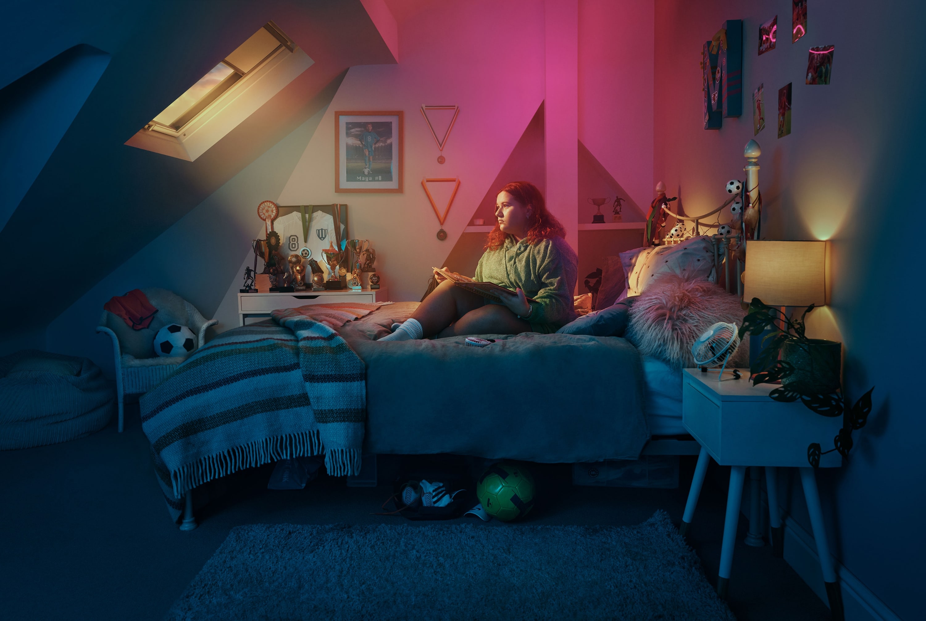 Girl sitting and holding a book in soccer-themed bedroom. Actor portrayal.